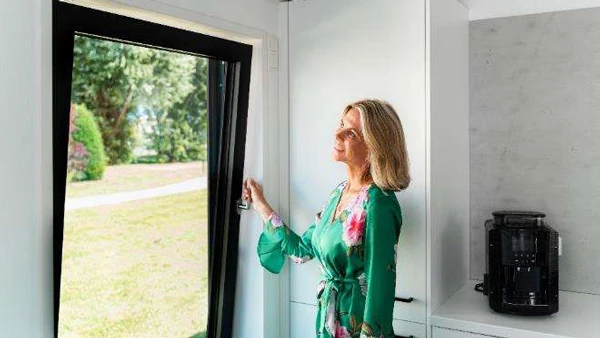Frau öffnet ein motorisiertes Fenster per Knopfdruck und sorgt für komfortable Lüftung im modernen Wohnraum.